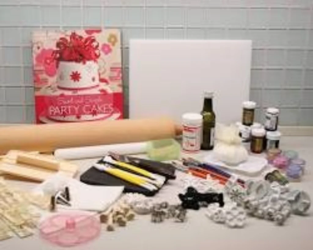Collection of cake decorating supplies: a book, rolling pins, sculpting tools, food colors, and molds.