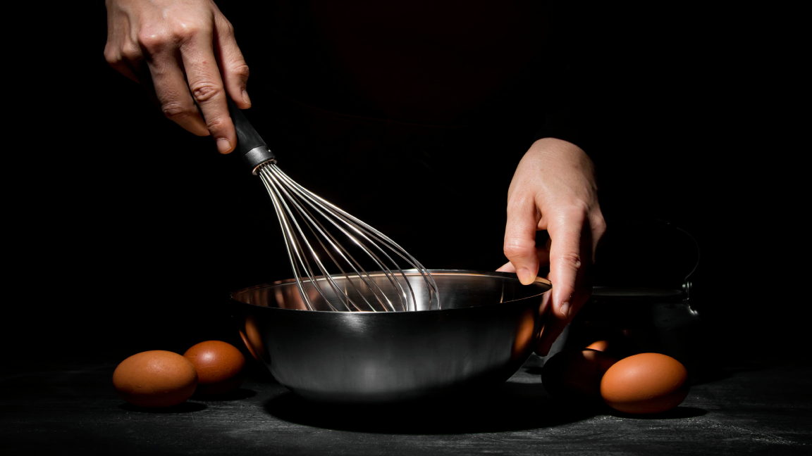hands whisking eggs in a stainless steel bowl