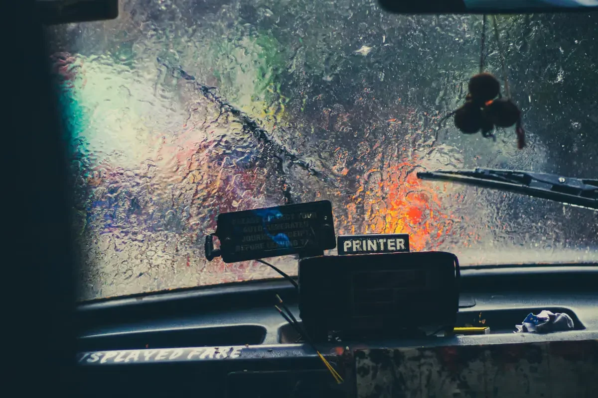 Blurry view through a rain-covered car windshield with city lights visible.